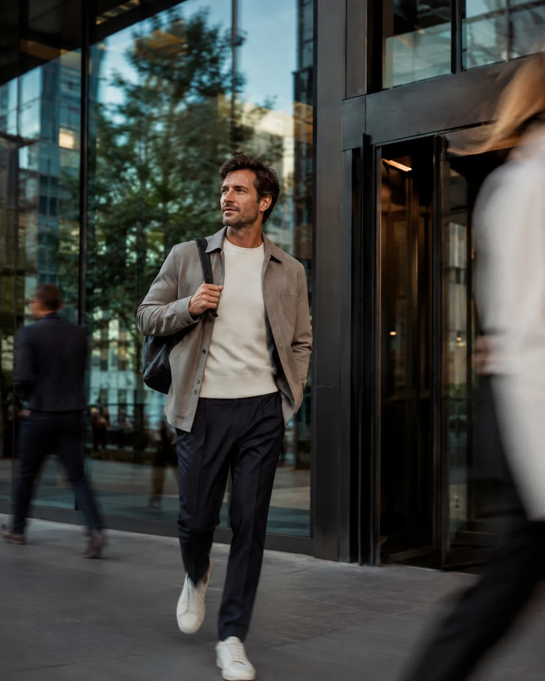 A man carrying a shoulder bag outside a glass-fronted building
